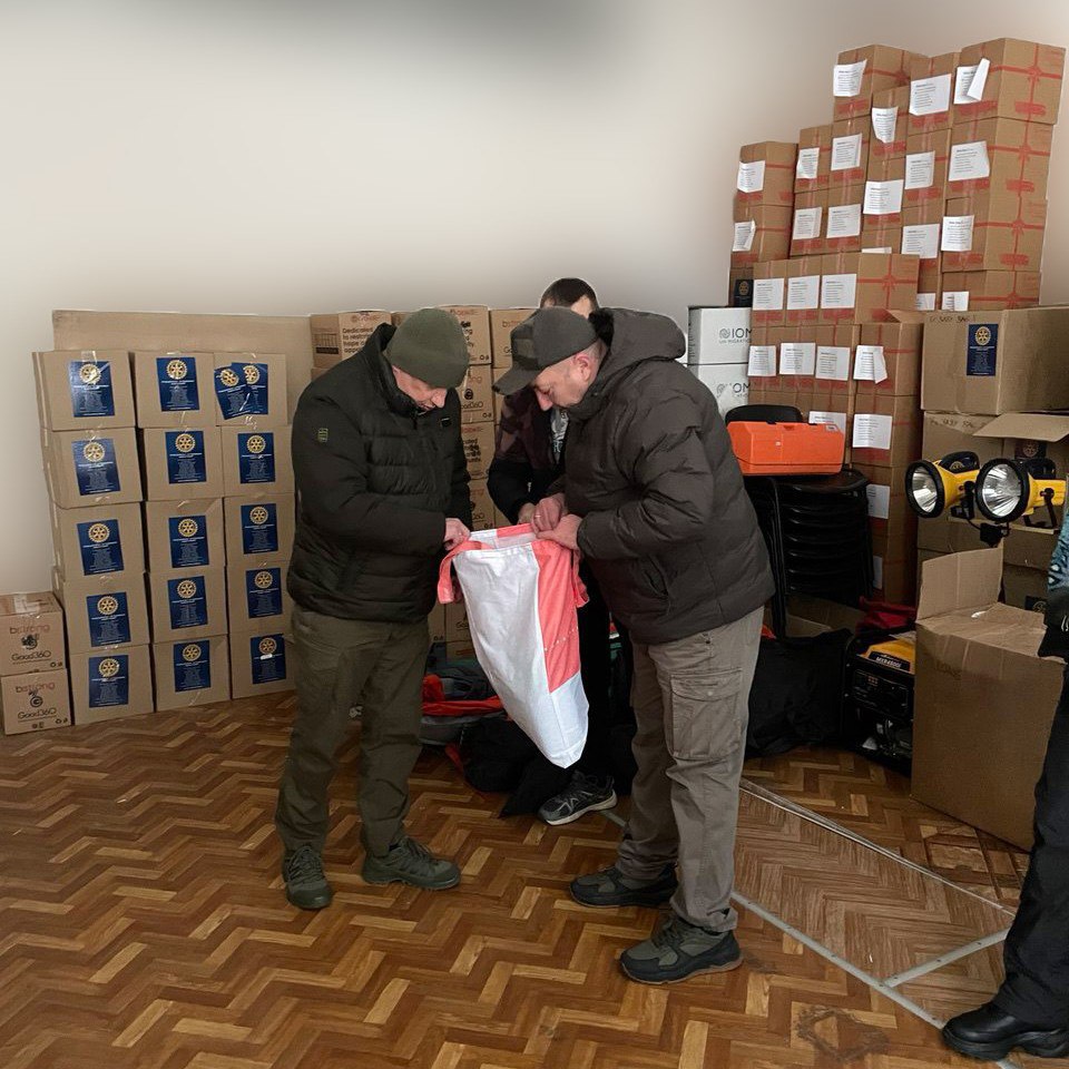 Двоє чоловіків на складі схилилися над великим біло-рожевим мішком, оглядаючи його вміст на фоні стосів коробок.