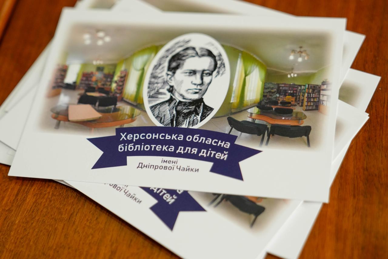 Стос листівок Херсонської обласної бібліотеки для дітей імені Дніпрової Чайки. На листівці зображено портрет письменниці на фоні інтер'єру сучасної бібліотечної зали з книжковими полицями та столами.