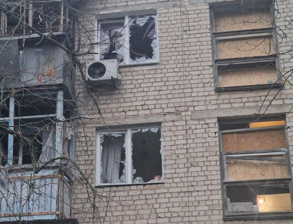 Фасад цегляного багатоповерхового будинку з пошкодженими балконами та вибитими шибками. Частина вікон уже забита листами фанери або ОСБ-плитами.