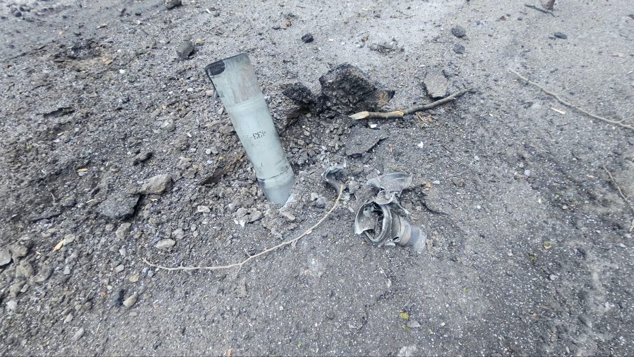 Нерозірваний хвостовик боєприпасу, що влучив у землю та застряг в асфальтовому покритті серед дрібних уламків і каміння.