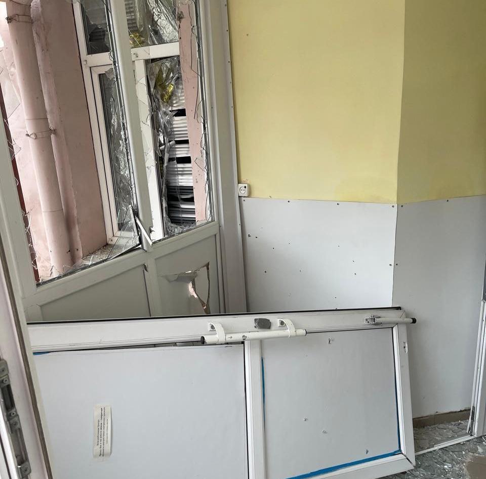 Наслідки вибухової хвилі всередині приміщення: вибиті металопластикові двері та розтрощене скло, що лежить на підлозі поруч із пошкодженою стіною.