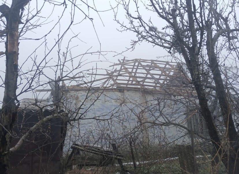 Дерев'яний каркас даху будівлі без покрівлі, що видніється крізь голі гілки дерев у туманну або похмуру погоду.