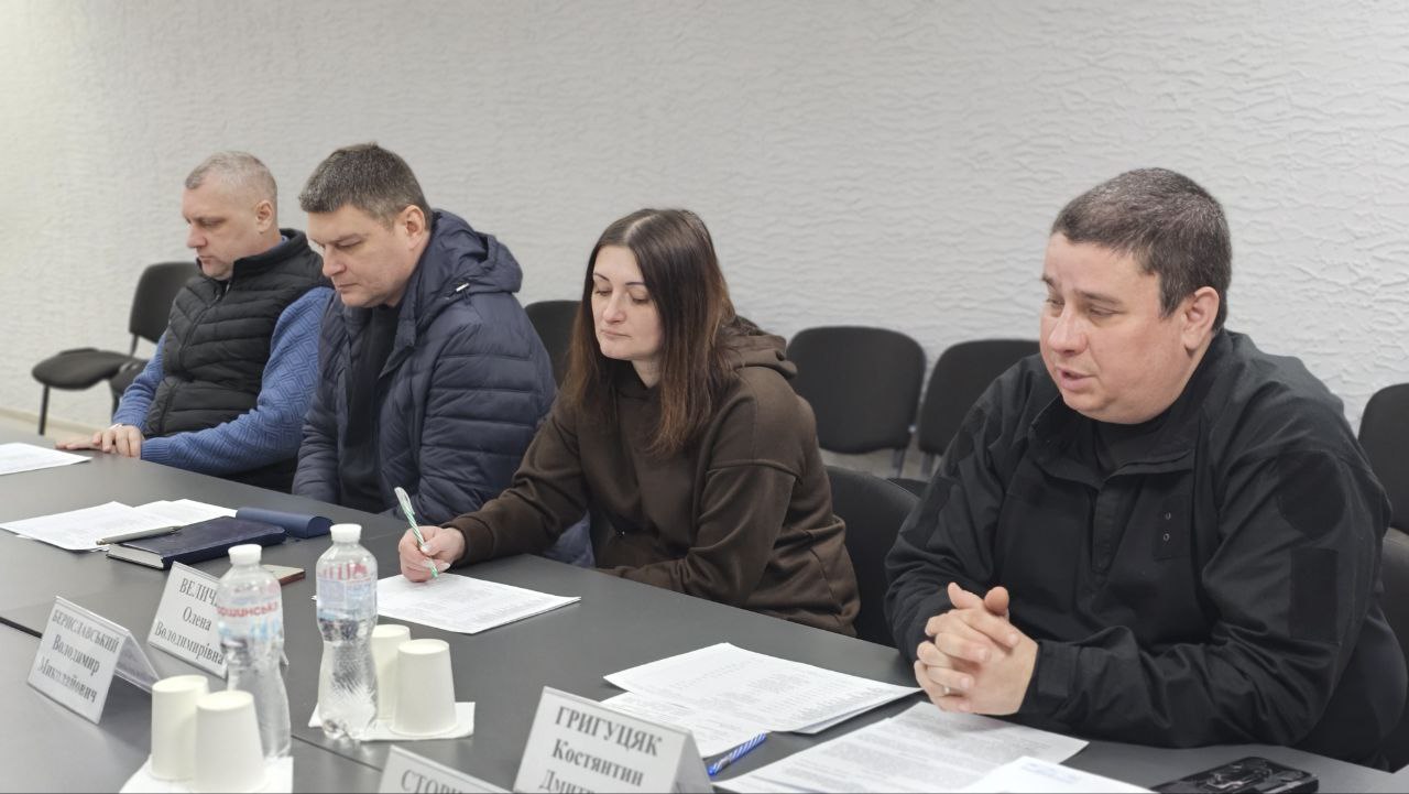 Учасники робочої зустрічі в офіційному приміщенні сидять за столом, вивчають документи та роблять нотатки.