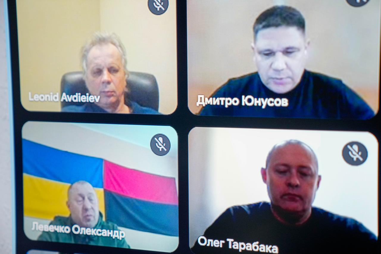 Скриншот відеодзвінка з чотирма учасниками. Чоловіки мають зосереджений вигляд; один із них перебуває на фоні українського та червоно-чорного прапорів. Під кожним вікном відеозв'язку вказано ім'я та прізвище.