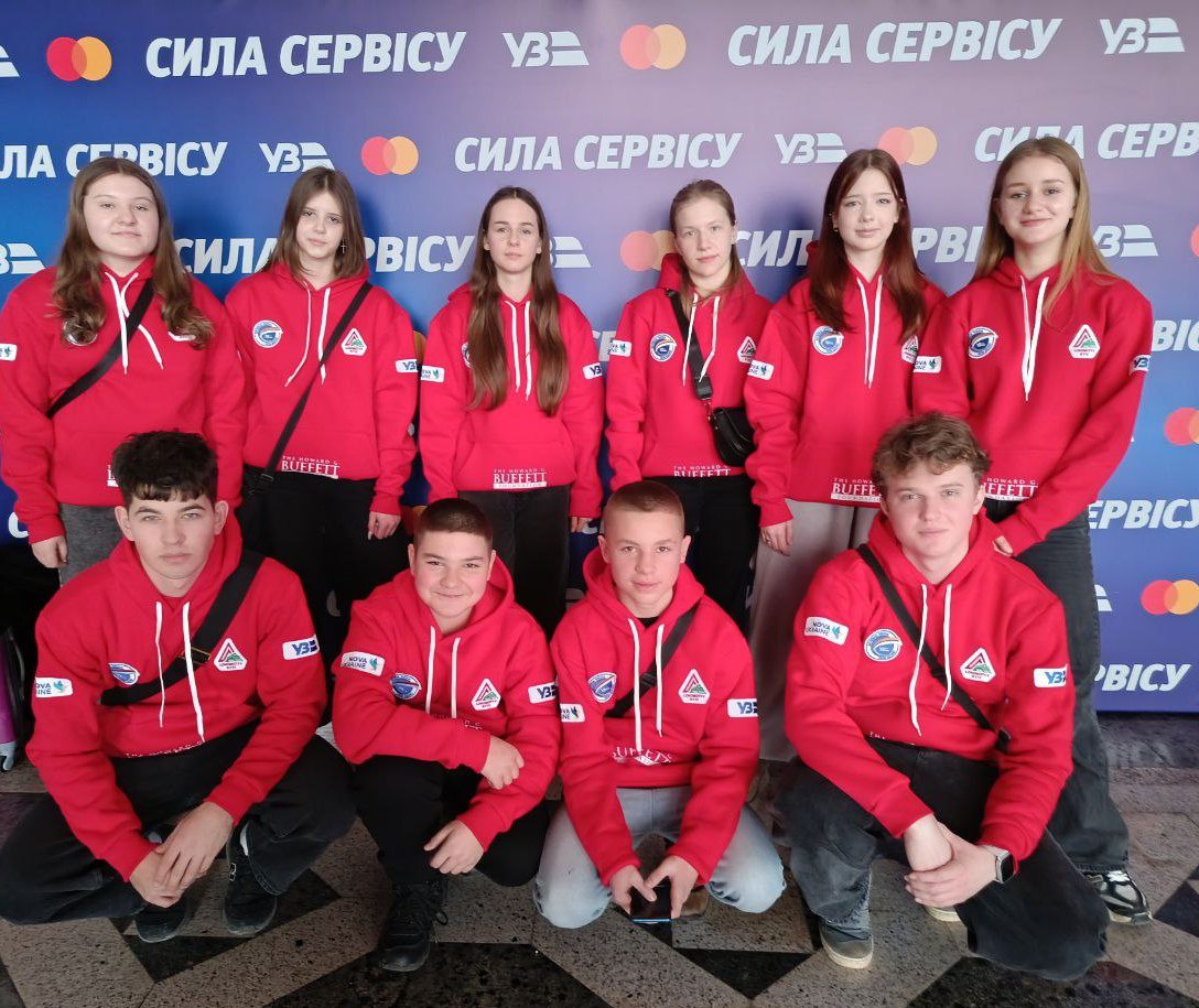 Групове фото десяти підлітків, які позують на фоні банера з написом «Сила сервісу» та логотипами «Укрзалізниці» та Mastercard. Усі учасники одягнені в однакові червоні худі з нашивками організацій-партнерів. Чотири хлопці сидять на передньому плані, а шість дівчат стоять позаду них.