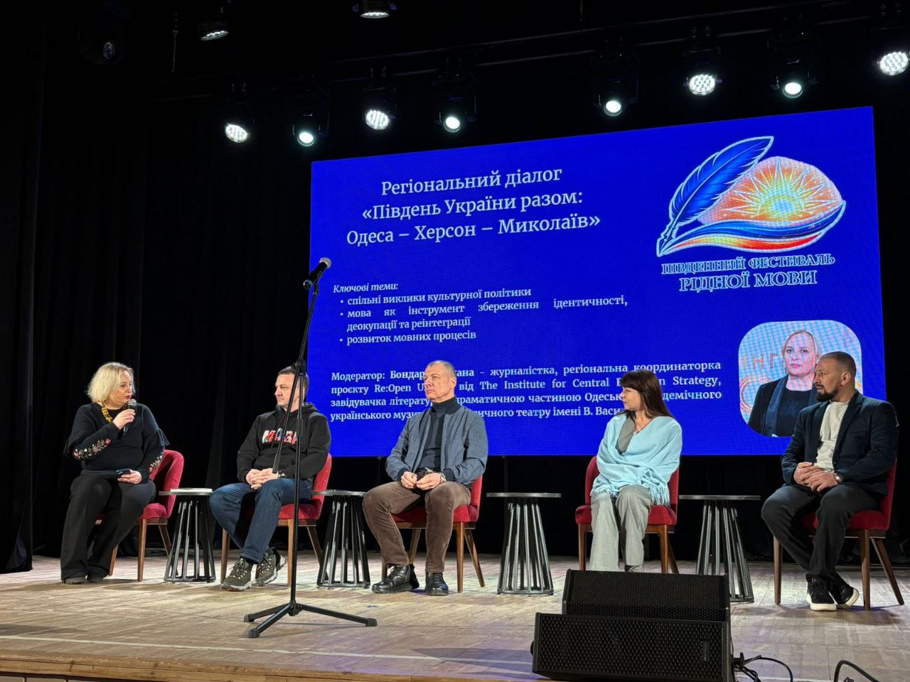П'ятеро спікерів беруть участь у панельній дискусії на сцені під час заходу «Регіональний діалог "Південь України разом: Одеса — Херсон — Миколаїв"». Учасники сидять у кріслах на фоні великого синього екрана з тезами обговорення та логотипом «Південний фестиваль рідної мови».