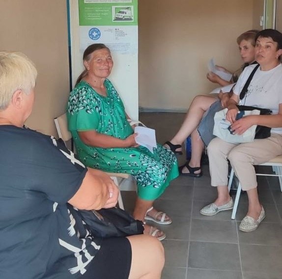 Пацієнти на Херсонщині очікують на прийом лікарів мобільної бригади ГО «CASERS» у коридорі медичного закладу. Кілька жінок сидять на стільцях із паперами в руках, на задньому плані видно інформаційний плакат організації.