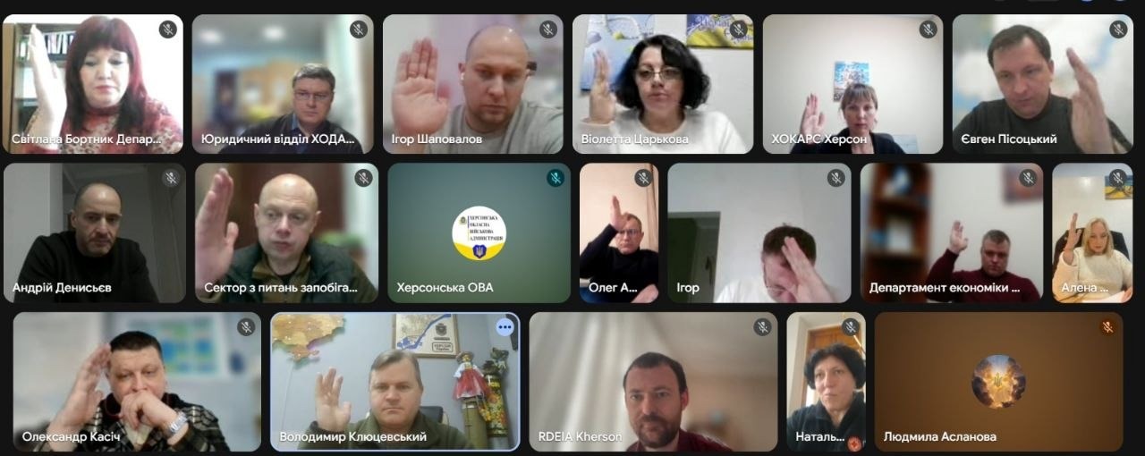 Скриншот онлайн-наради у форматі відеоконференції. На екрані видно вікна багатьох учасників, більшість з яких тримають підняту руку під час голосування; по центру розташований логотип Херсонської ОВА.